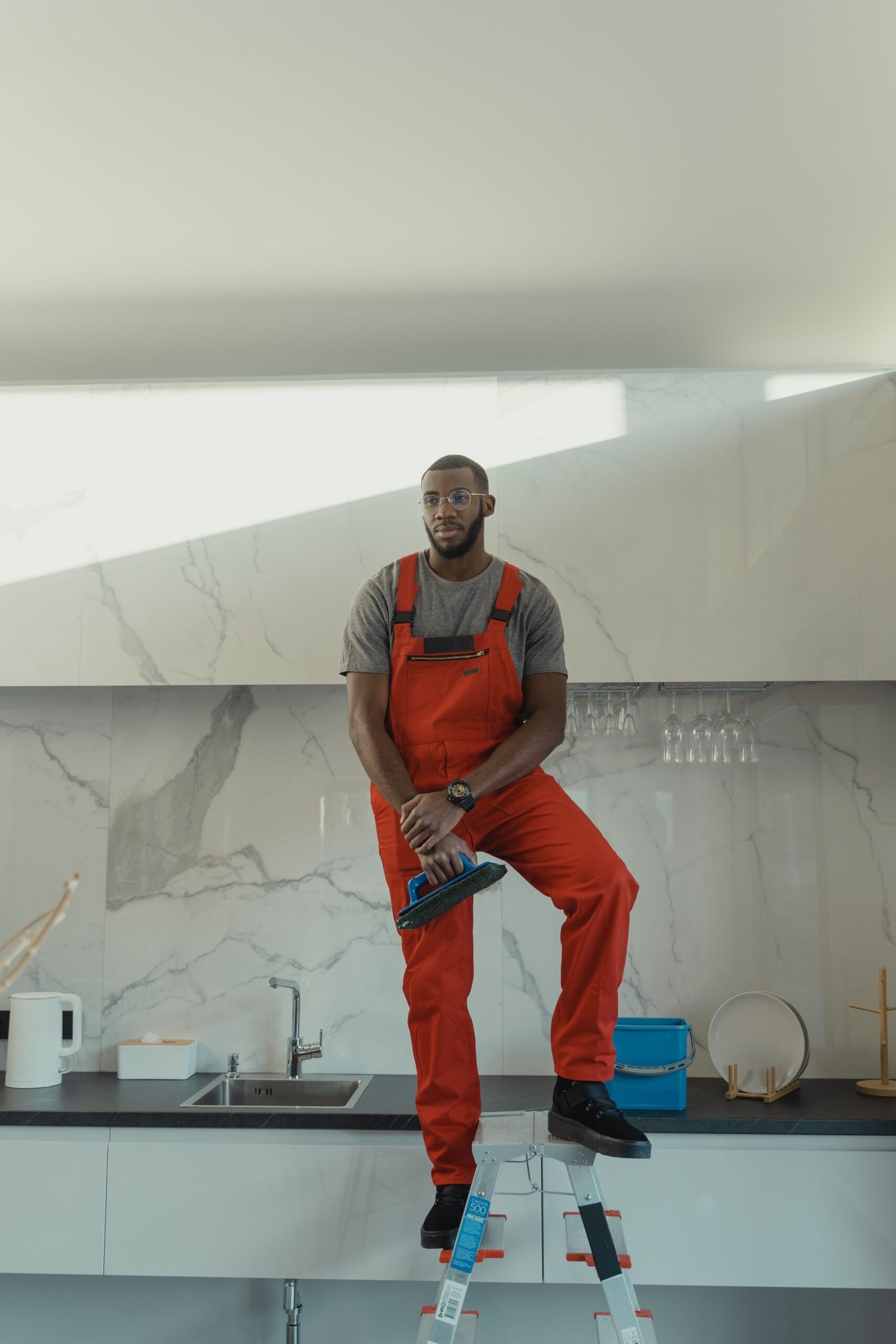 Man in red overalls standing on ladder cleaning modern kitchen.